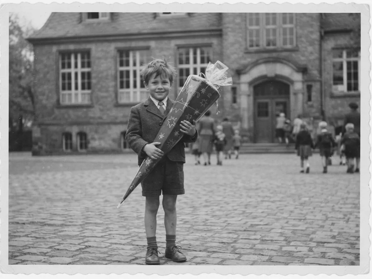 Ein Schwarz-Weiß-Foto eines Jungen mit Schultüte vor der Schule